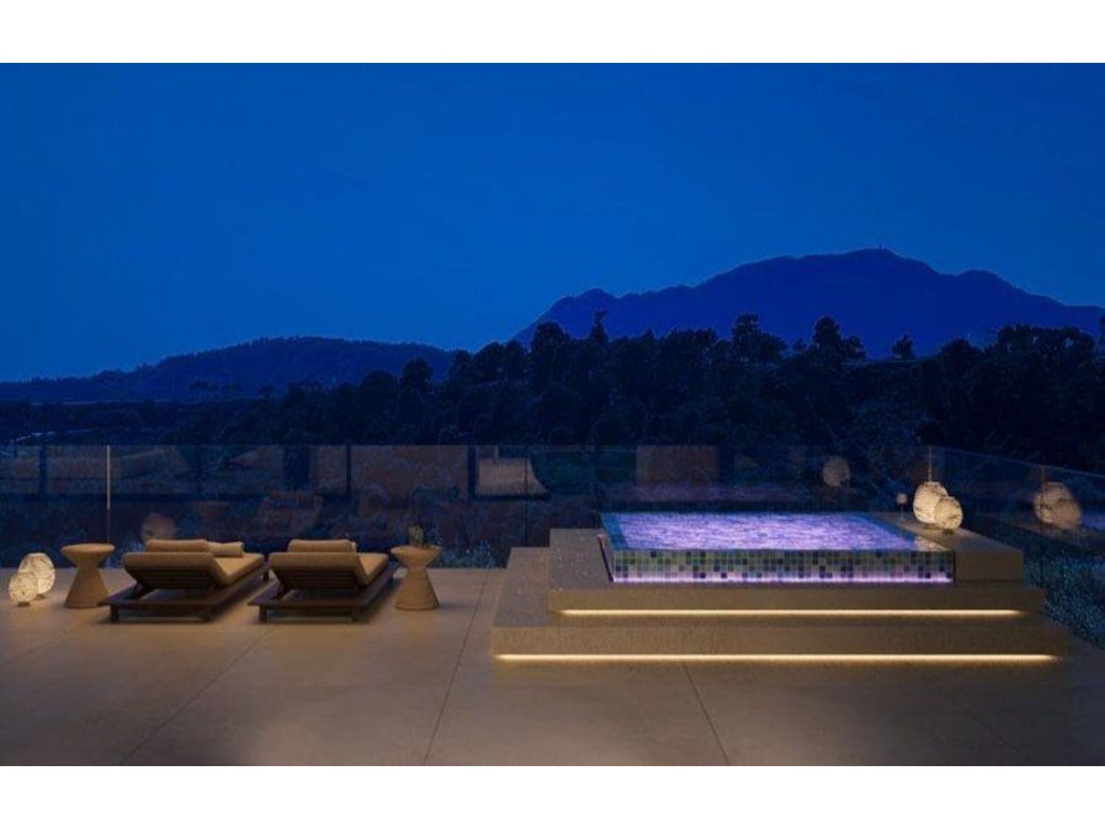 Outdoor terrace with pool, lounge chairs, and mountain view at night.